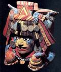 Керамическая коробка в виде некоего божества, стоящего вверх ногами, говорит о влиянии иных мезоамериканских культур на позднейшее искусство майя. Об этом можно судить по пятнам, какие бывают на шкуре ягуара, и по цветным полосам на лице. Считается, что это изображение бога кукурузы, он держит в руках обычную пищу майя — тамали из кукурузы